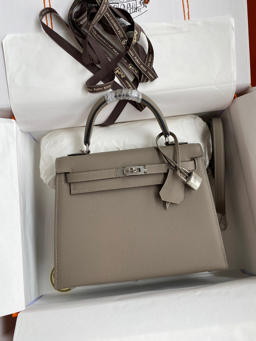 Gray handbag with a silver clasp in an open white box
