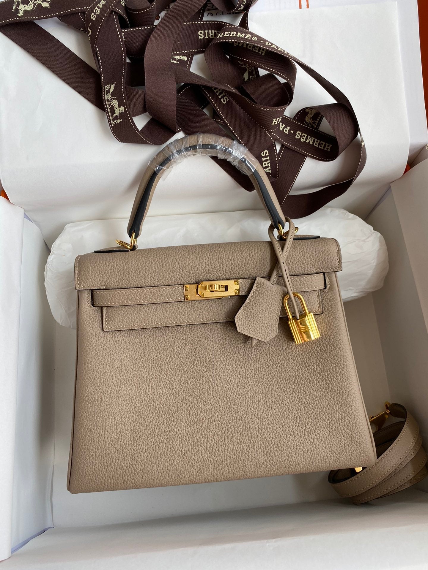 Beige handbag with gold hardware in a white box, featuring Hermès branding.