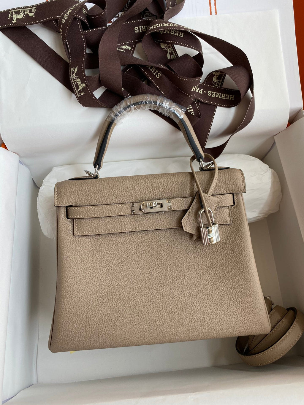 Beige handbag with a matching strap in a white box