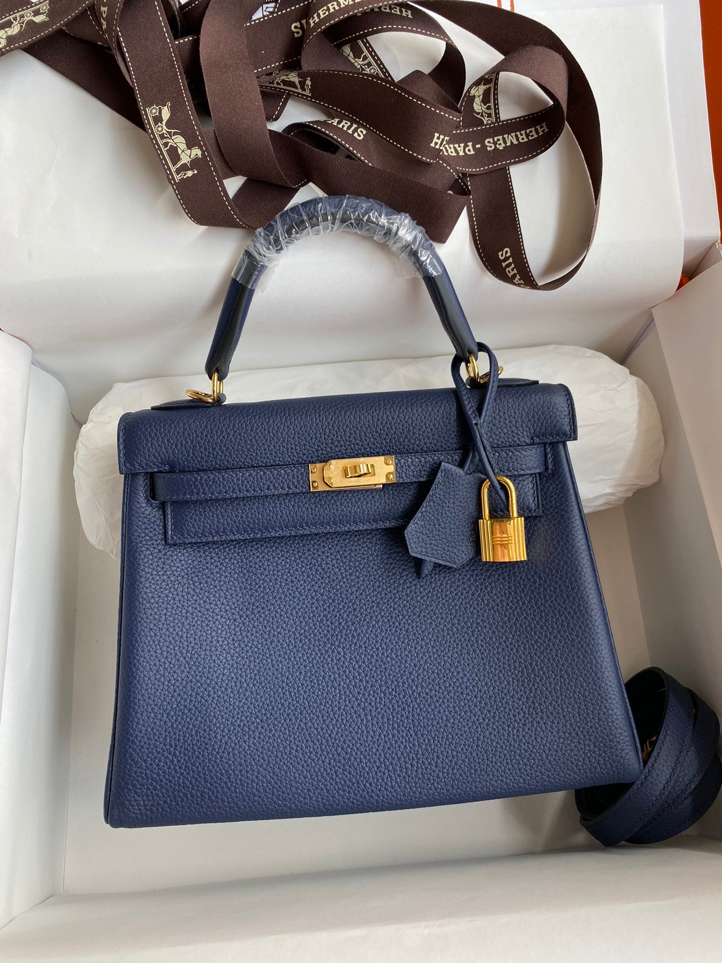 Blue handbag with gold hardware in a white box, featuring Hermès branding.