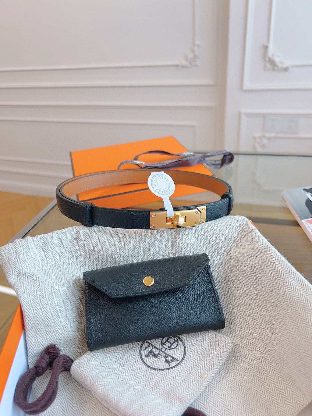 Black leather wallet with gold button on a white cloth, with an orange box in the background.