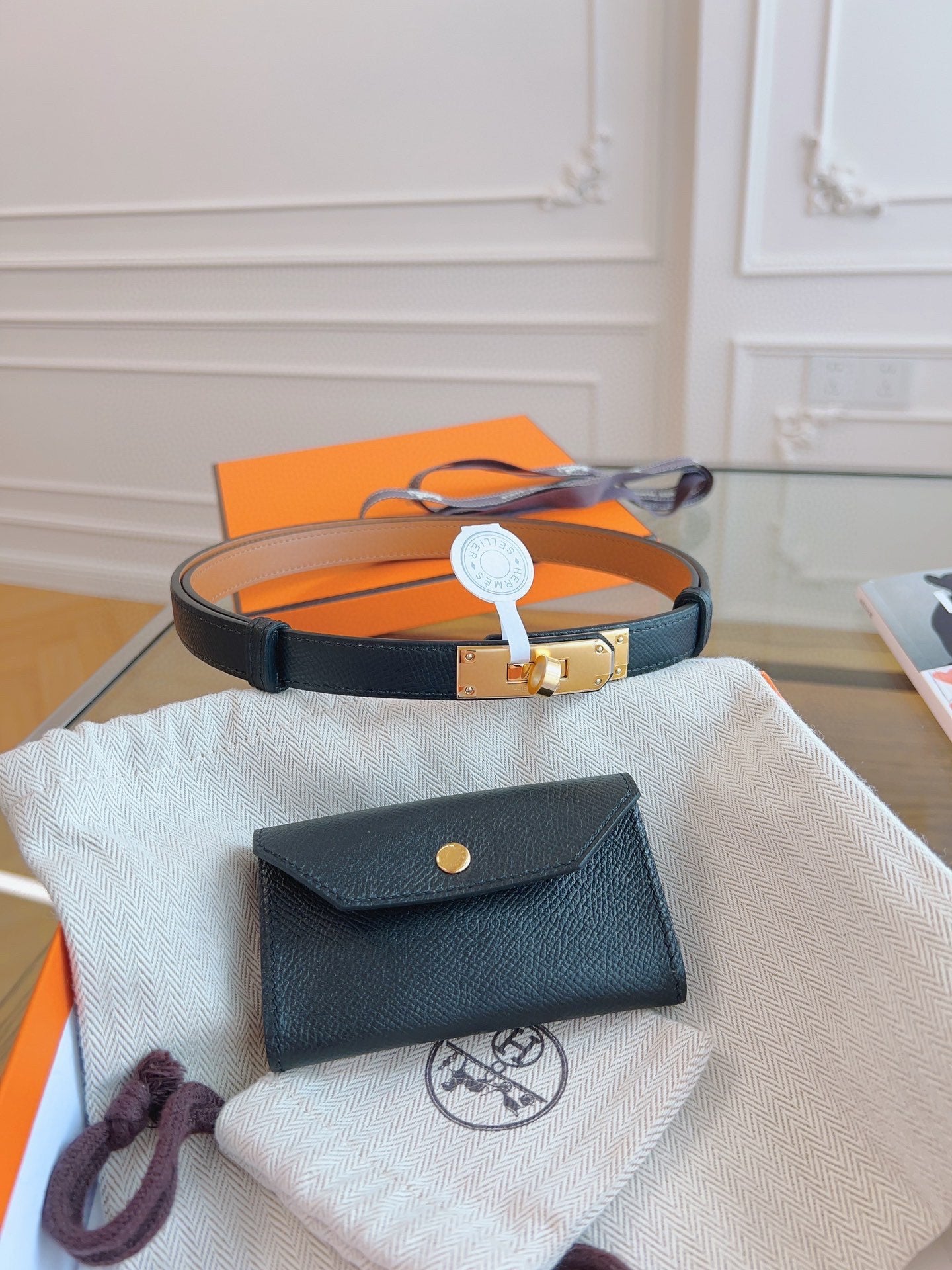 Black leather wallet with gold button on a white cloth, with an orange box in the background.