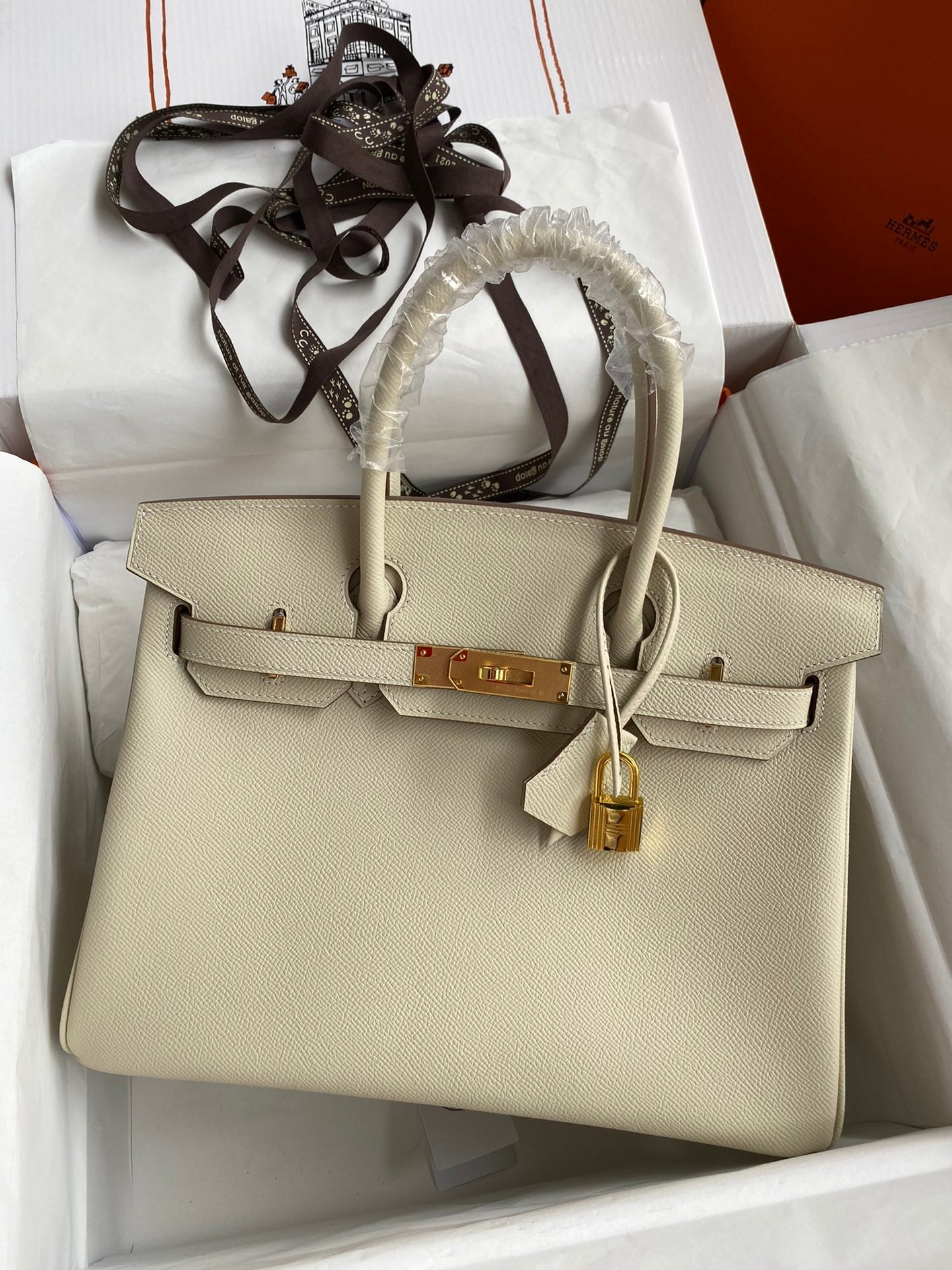 Beige handbag with gold hardware on a white surface