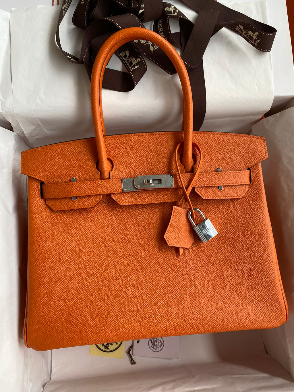 Orange handbag with a silver lock on a white surface