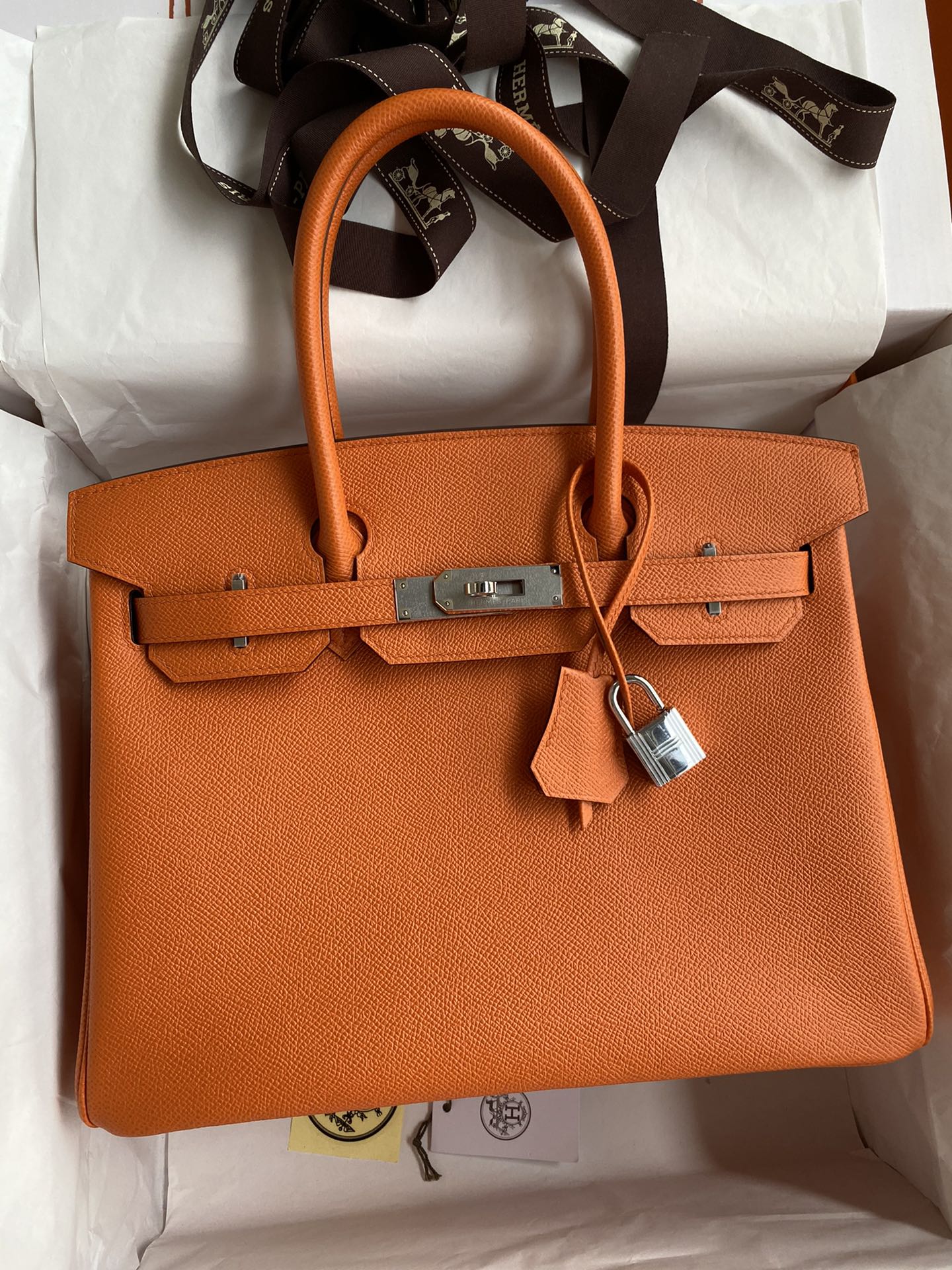 Orange handbag with a silver lock on a white surface