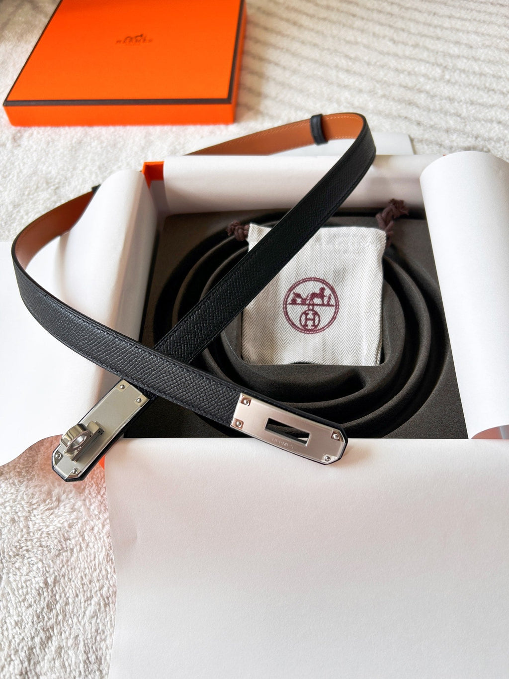 Black belt with silver buckle on a white surface, with an orange box in the background.