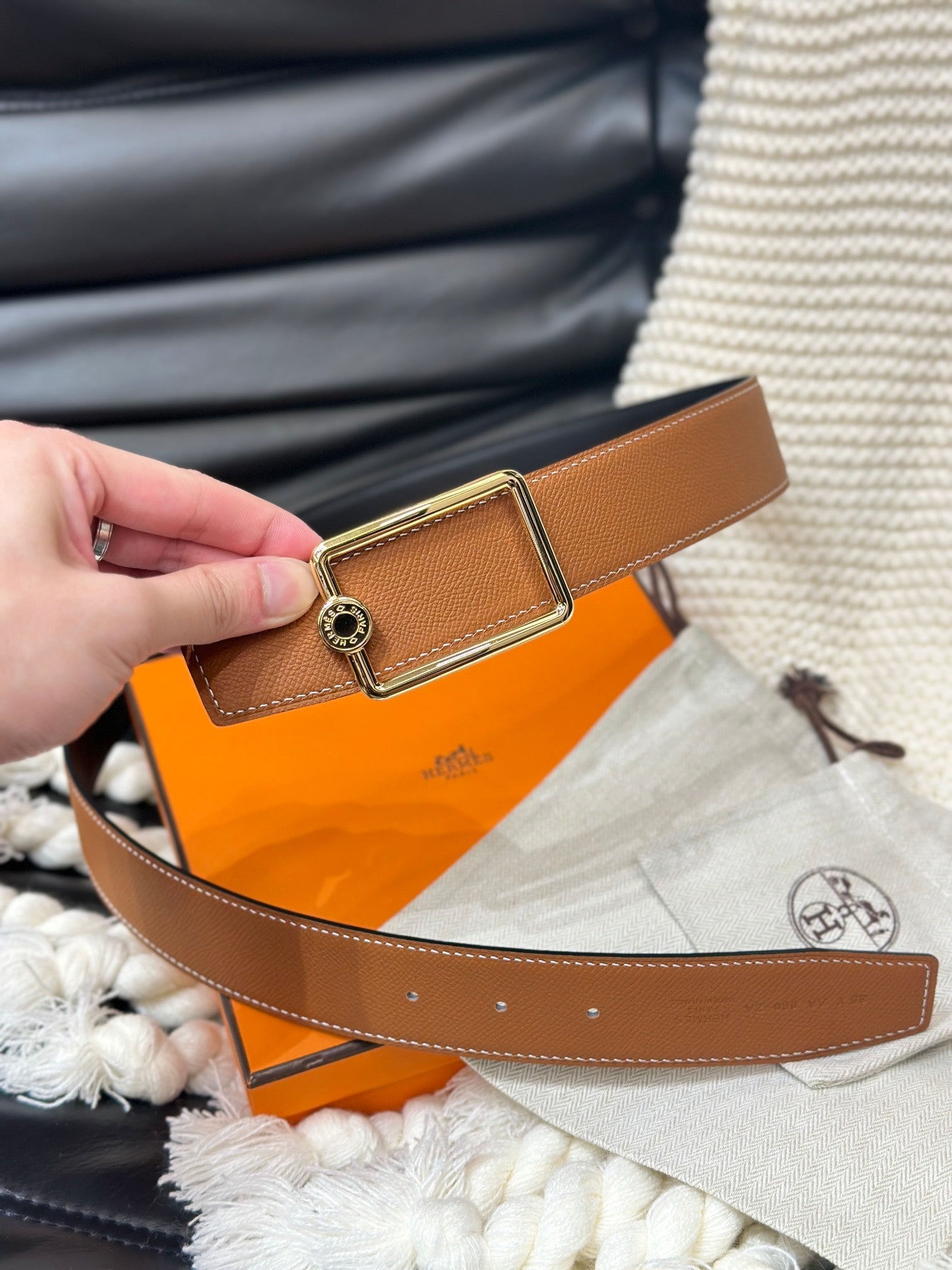 Brown belt with gold buckle being worn over an orange Hermes bag.