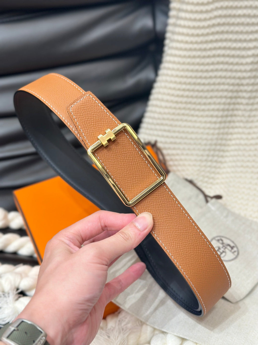 Brown belt with gold buckle held by a hand against a blurred background