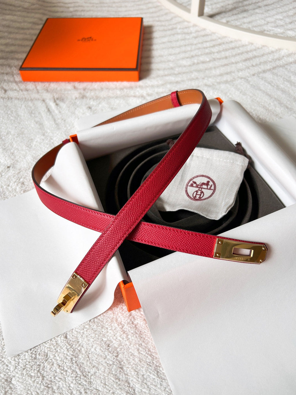 Red belt with gold buckle on a white surface, with an orange box in the background.