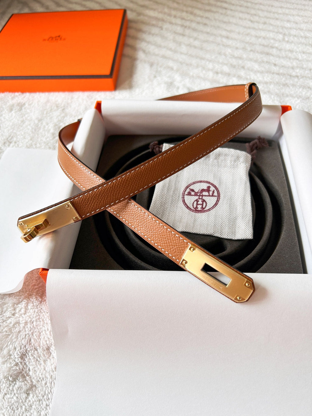Brown leather belt with gold buckle in a box, featuring Hermès logo.
