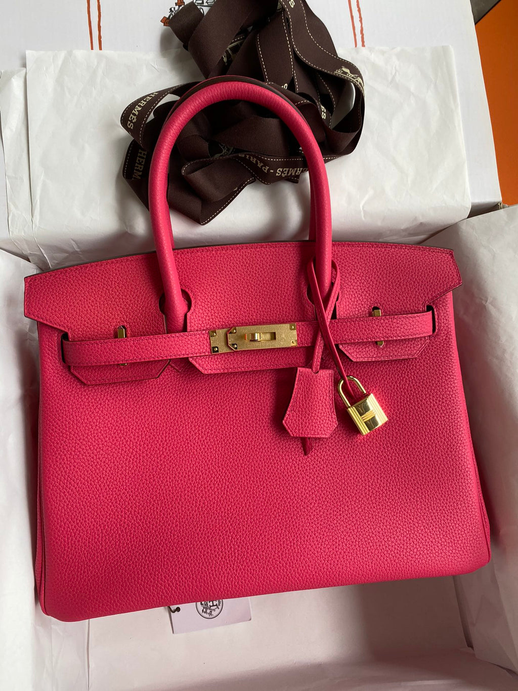 Pink handbag with gold hardware on a white surface