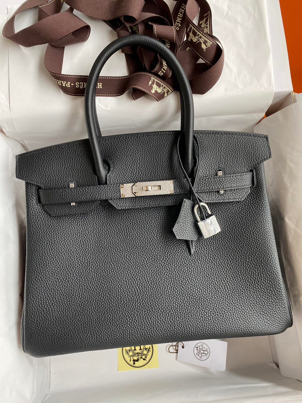 Gray handbag with silver hardware on a white surface, surrounded by brown ribbons.