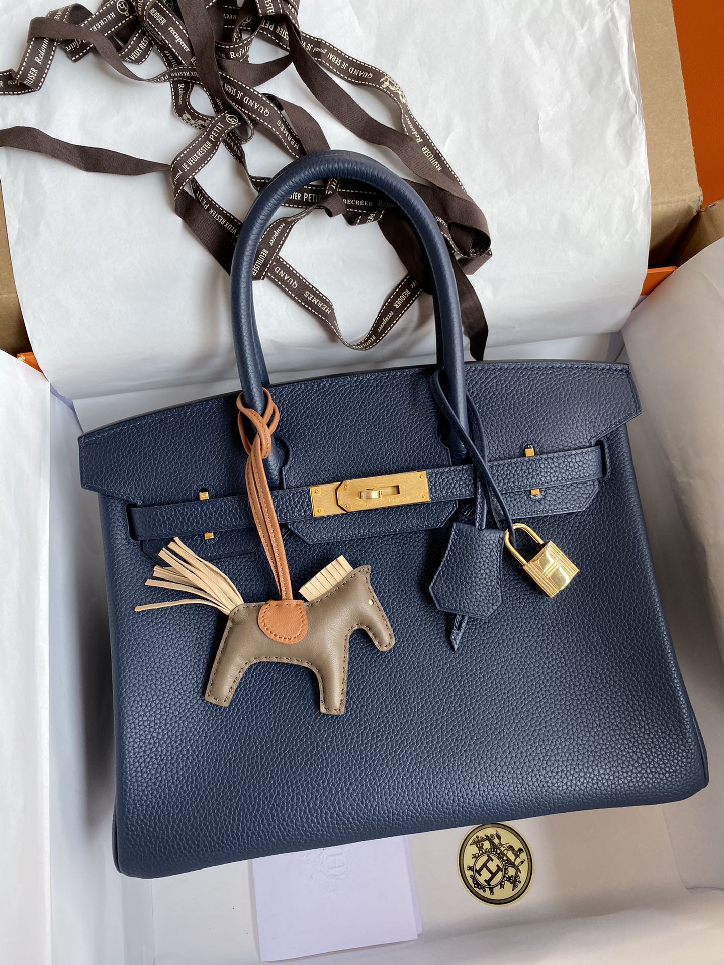 Blue handbag with gold hardware and a horse charm on a white background