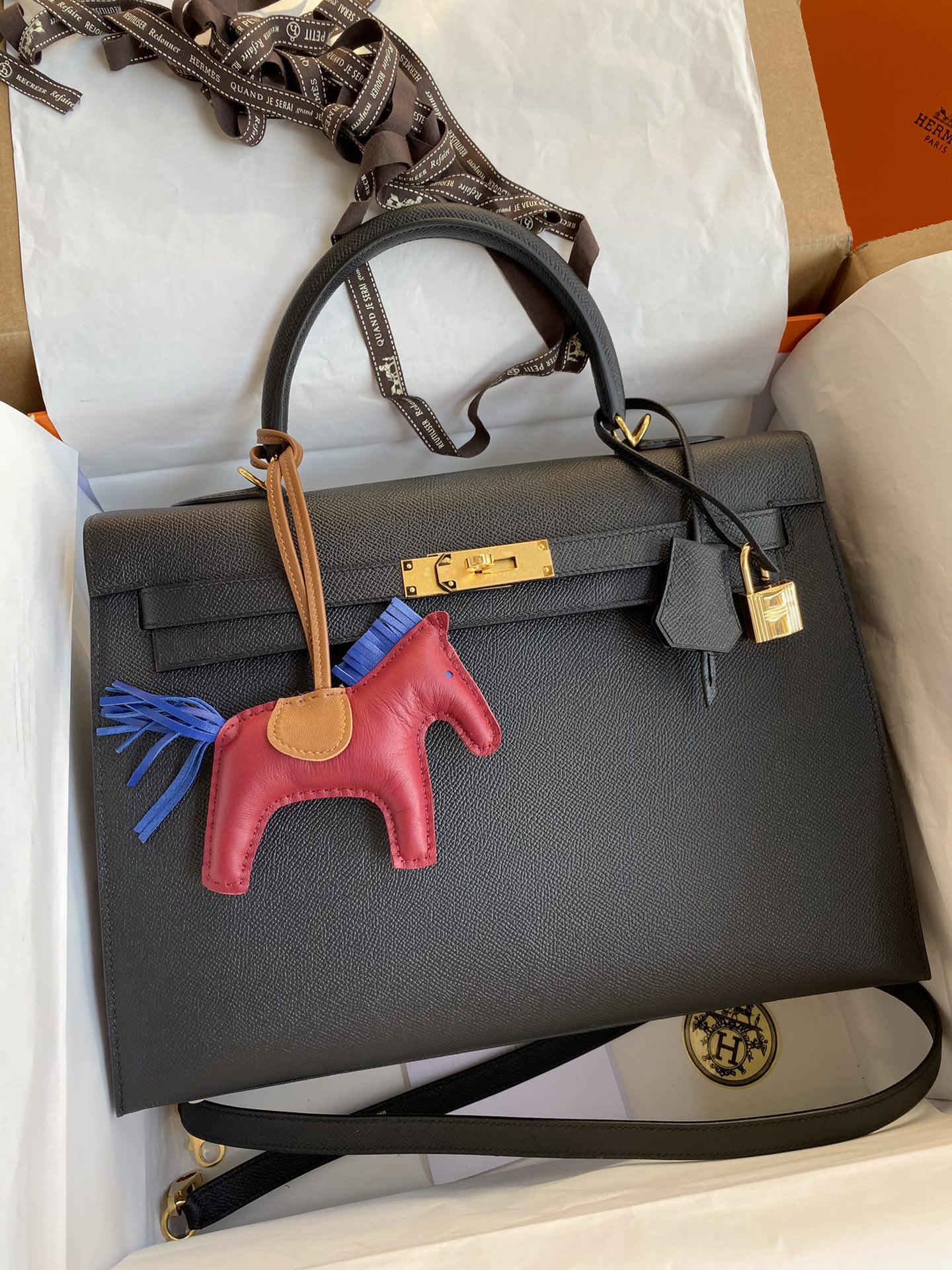 Black handbag with a red and blue horse charm on a white surface
