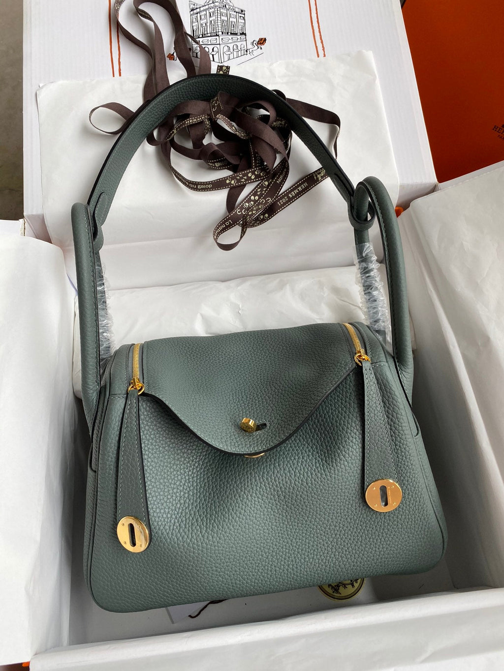 Green handbag with gold accents in a white box