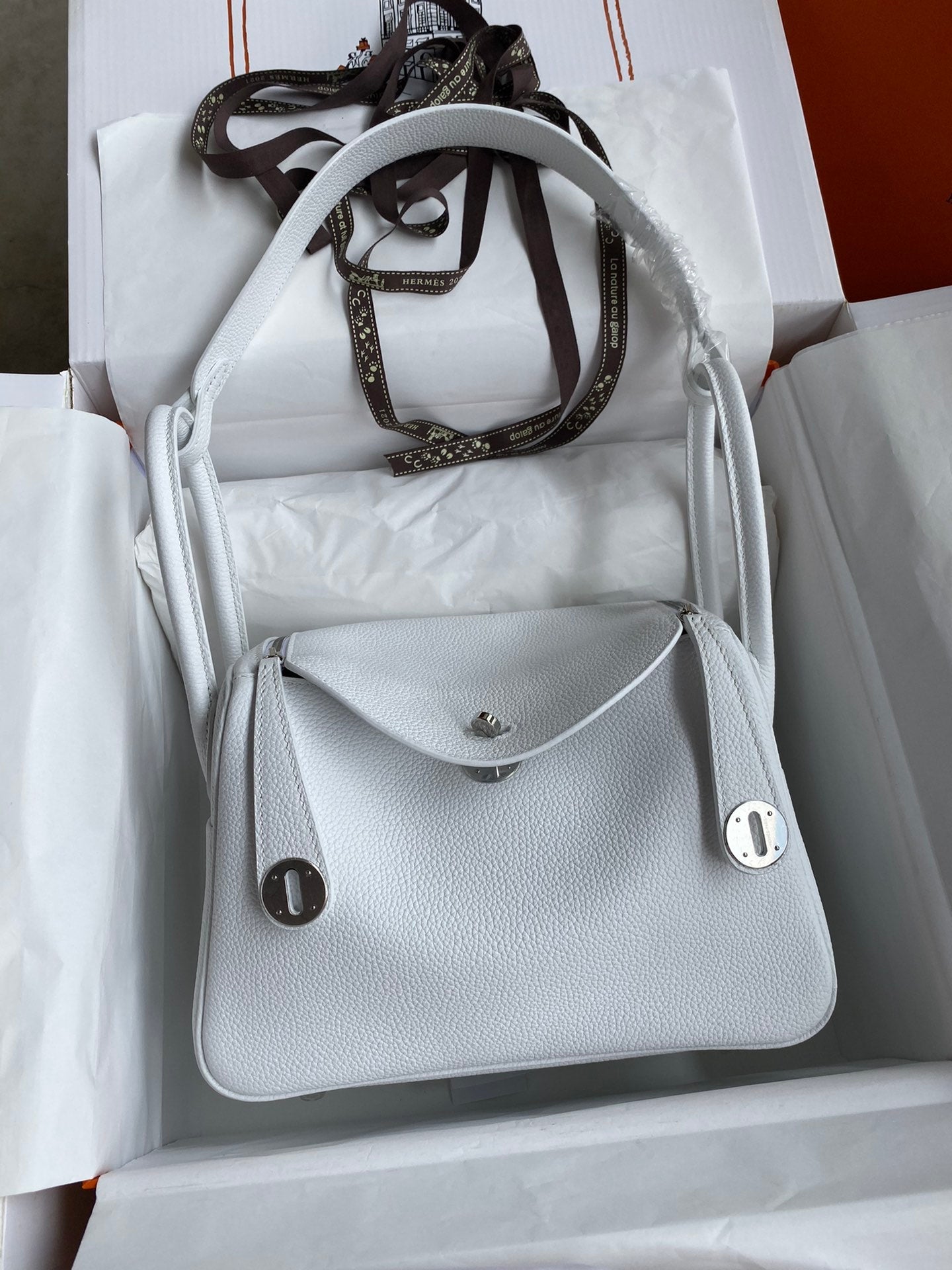 White handbag with brown strap in a white box
