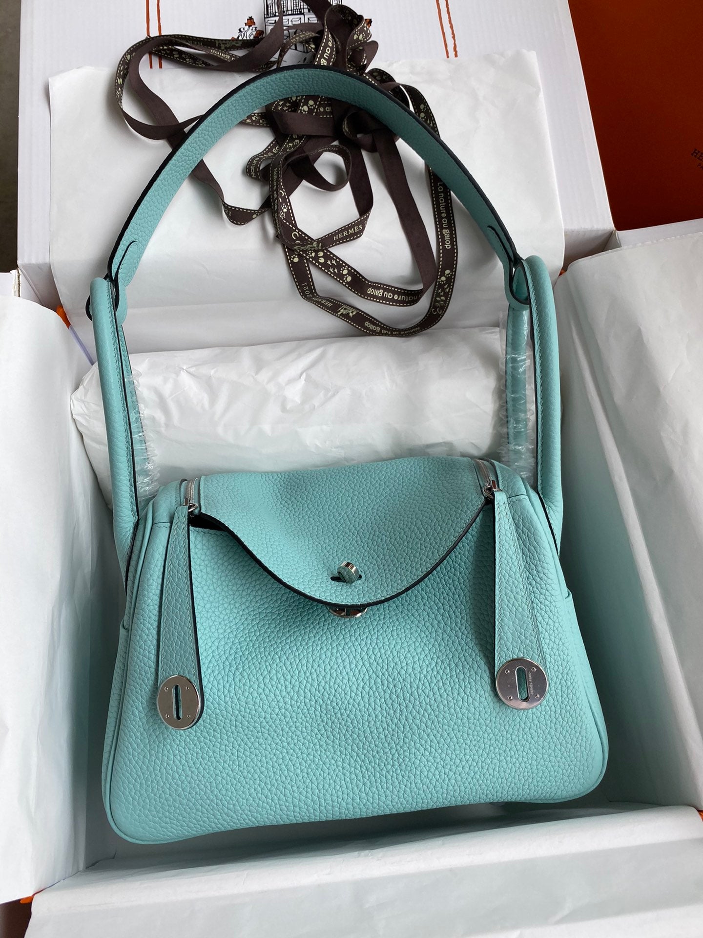 Turquoise handbag in a white box with a brown strap.