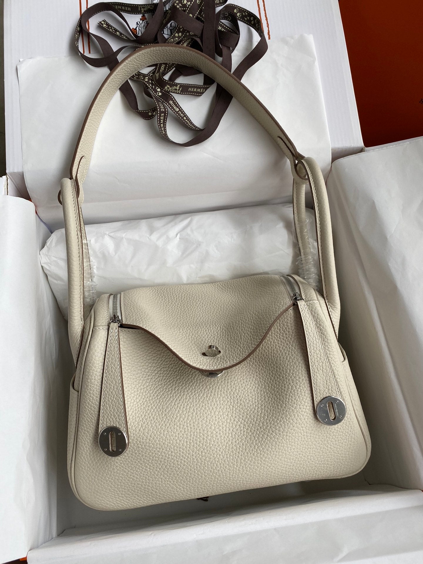 Beige handbag in a white box with a visible brand logo.